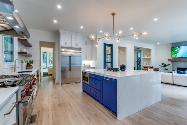 3449 Potomac Ave, Highland Park, TX 75205 - kitchen featuring high quality appliances, island range hood, white cabinetry, light wood-style flooring, and blue cabinetry