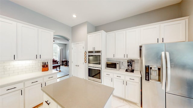 3009 Wood Trl, Flower Mound, TX 75022 - kitchen featuring appliances with stainless steel finishes, arched walkways, tasteful backsplash, white cabinetry, and a kitchen island