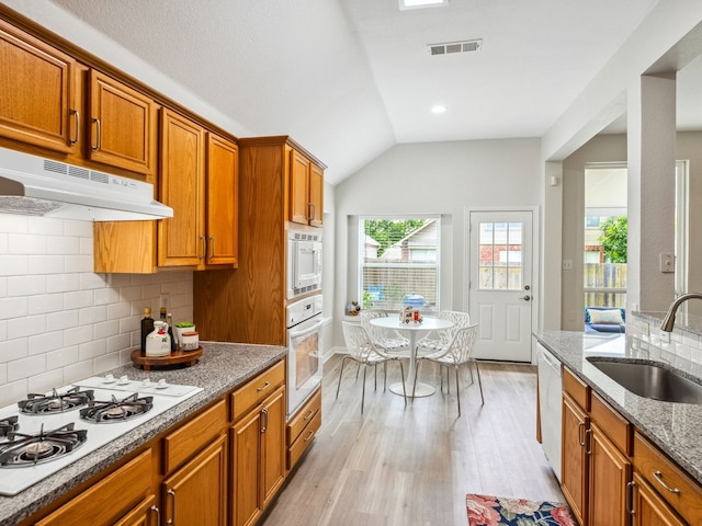 5117 Forest Lawn Dr, Mckinney, TX 75071 - kitchen with white appliances, under cabinet range hood, brown cabinetry, light wood-type flooring, and vaulted ceiling
