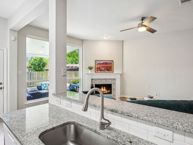 5117 Forest Lawn Dr, Mckinney, TX 75071 - kitchen featuring light stone counters, a tiled fireplace, a ceiling fan, and open floor plan