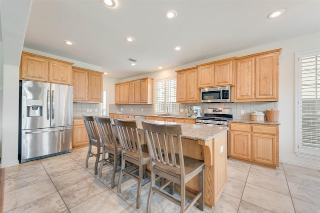 1021 Springtown St, Forney, TX 75126 - kitchen featuring appliances with stainless steel finishes, a center island, decorative backsplash, light brown cabinetry, and recessed lighting
