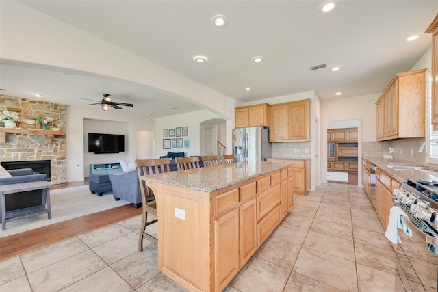 1021 Springtown St, Forney, TX 75126 - kitchen with stainless steel appliances, light brown cabinetry, a breakfast bar area, arched walkways, and light stone countertops