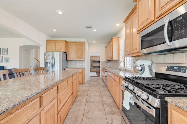 1021 Springtown St, Forney, TX 75126 - kitchen featuring appliances with stainless steel finishes, light brown cabinets, backsplash, light stone countertops, and arched walkways