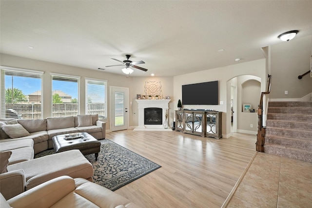 10704 Parnell Dr, Mckinney, TX 75072 - living area featuring arched walkways, a ceiling fan, stairs, light wood-type flooring, and a glass covered fireplace