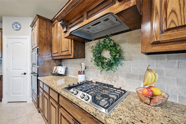 10704 Parnell Dr, Mckinney, TX 75072 - kitchen with stainless steel appliances, ventilation hood, light stone counters, tasteful backsplash, and brown cabinets