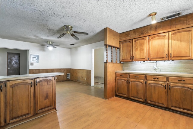 221 E 7th St, Weatherford, TX 76086 - kitchen with light wood-style flooring, brown cabinets, wainscoting, light countertops, and ceiling fan
