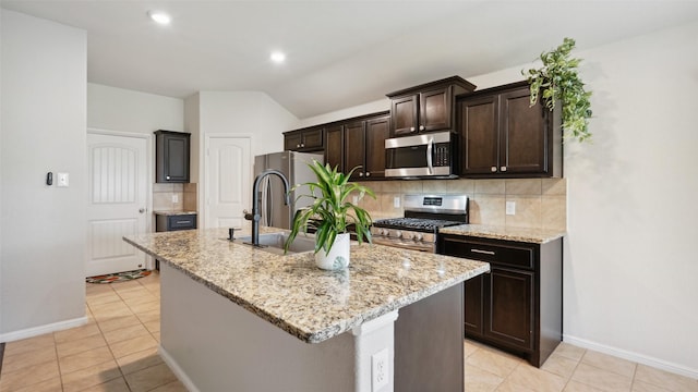 6348 Porthole Ln, Fort Worth, TX 76179 - kitchen featuring appliances with stainless steel finishes, backsplash, an island with sink, dark brown cabinets, and vaulted ceiling
