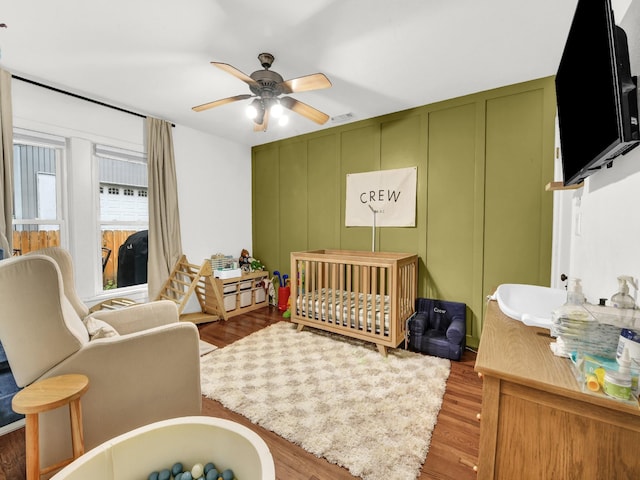 3921 Bryce Ave, Fort Worth, TX 76107 - bedroom featuring a decorative wall, a nursery area, wood finished floors, and ceiling fan