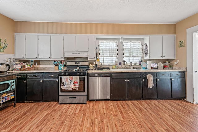 814 N Ollie St, Stephenville, TX 76401 - kitchen featuring appliances with stainless steel finishes, under cabinet range hood, light wood finished floors, white cabinetry, and a textured ceiling