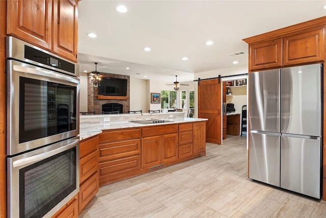 750 Emerald Sound Blvd, Oak Point, TX 75068 - kitchen with appliances with stainless steel finishes, ceiling fan, a fireplace, a peninsula, and a barn door