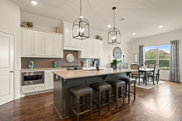 1105 Denton Creek Dr, Justin, TX 76247 - kitchen with stainless steel microwave, decorative backsplash, dark wood finished floors, an island with sink, and a chandelier