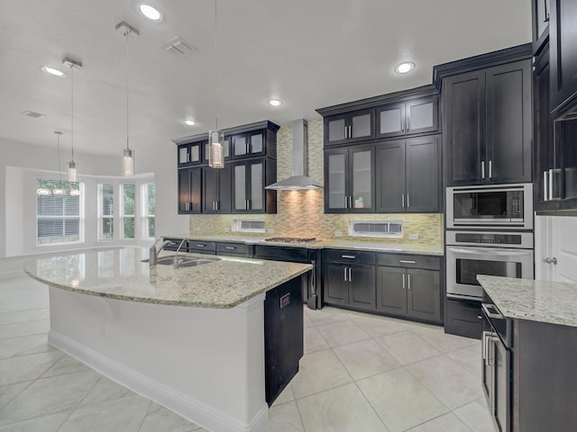 12815 Lourdes Ln, Frisco, TX 75035 - kitchen featuring stainless steel appliances, wall chimney exhaust hood, decorative backsplash, a kitchen island with sink, and light stone counters