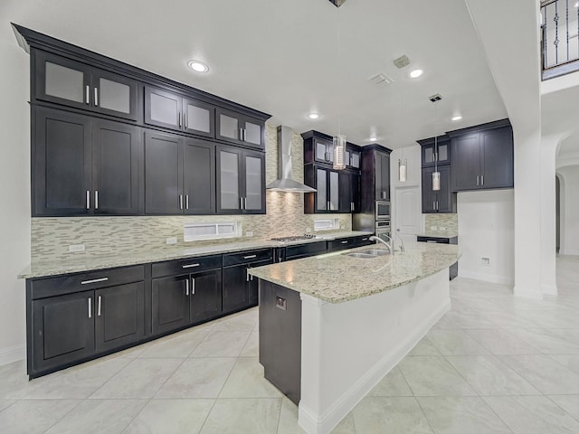 12815 Lourdes Ln, Frisco, TX 75035 - kitchen featuring wall chimney exhaust hood, arched walkways, stainless steel gas stovetop, tasteful backsplash, and light stone countertops