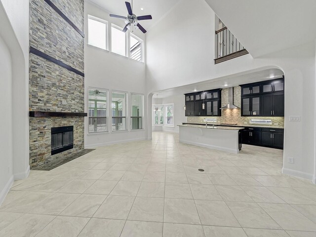 12815 Lourdes Ln, Frisco, TX 75035 - unfurnished living room featuring a ceiling fan, arched walkways, a stone fireplace, light tile patterned flooring, and a high ceiling