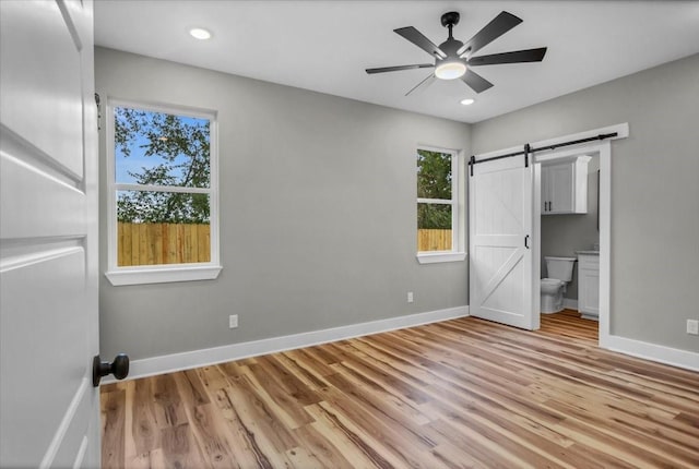1002 E Main, Whitehouse, TX 75791 - unfurnished bedroom featuring a barn door, light wood-type flooring, ensuite bathroom, recessed lighting, and ceiling fan
