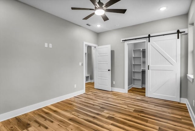 1002 E Main, Whitehouse, TX 75791 - unfurnished bedroom with wood finished floors, a barn door, a walk in closet, recessed lighting, and ceiling fan