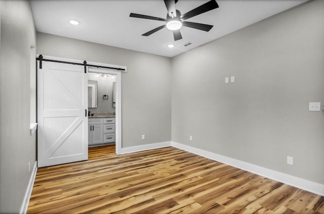 1002 E Main, Whitehouse, TX 75791 - unfurnished bedroom with a barn door, light wood-style floors, ensuite bathroom, recessed lighting, and ceiling fan
