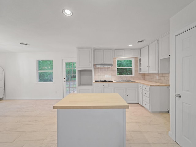 5537 Wheaton Dr, Fort Worth, TX 76133 - kitchen with a kitchen island, tasteful backsplash, white cabinetry, stainless steel gas cooktop, and under cabinet range hood
