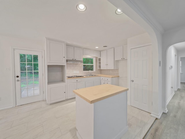 5537 Wheaton Dr, Fort Worth, TX 76133 - kitchen with stovetop, arched walkways, white cabinetry, backsplash, and under cabinet range hood
