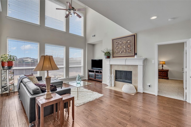 3537 Navarro Way, Frisco, TX 75034 - living room featuring a ceiling fan, plenty of natural light, a tiled fireplace, wood finished floors, and a towering ceiling