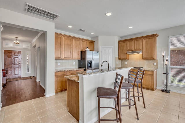 3537 Navarro Way, Frisco, TX 75034 - kitchen with stainless steel refrigerator with ice dispenser, under cabinet range hood, brown cabinets, light stone countertops, and recessed lighting