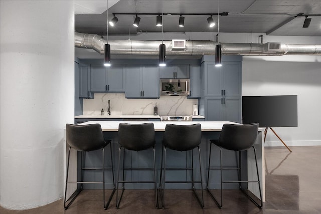 1122 Jackson St Unit 418, Dallas, TX 75202 - kitchen with stainless steel microwave, finished concrete flooring, light countertops, decorative backsplash, and a kitchen breakfast bar