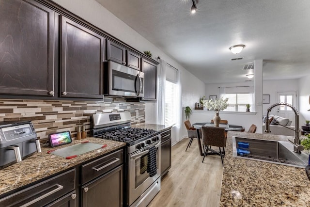 7113 Wavecrest Way, Fort Worth, TX 76179 - kitchen featuring stainless steel appliances, light wood-style flooring, backsplash, dark brown cabinets, and stone counters