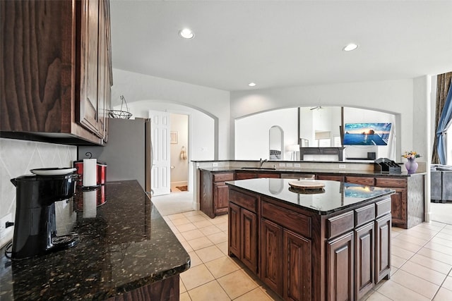 890 Wind Brook Ln, Prosper, TX 75078 - kitchen with arched walkways, a center island, light tile patterned floors, recessed lighting, and dark brown cabinets