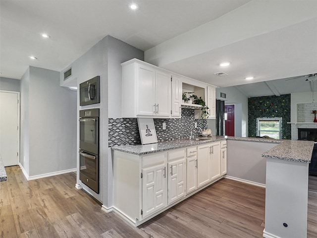 2032 Christie Ln, Carrollton, TX 75007 - kitchen with black microwave, a peninsula, wood finished floors, white cabinetry, and decorative backsplash