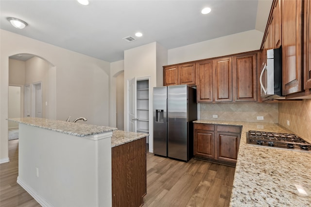 3408 Glen Crest Ln, Denton, TX 76208 - kitchen with appliances with stainless steel finishes, arched walkways, wood finished floors, decorative backsplash, and a center island with sink