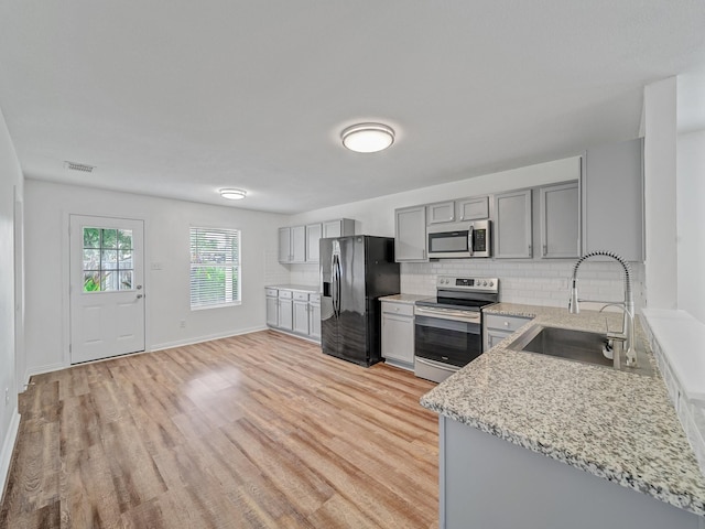 2321 Live Oak Dr, Little Elm, TX 75068 - kitchen featuring stainless steel appliances, gray cabinets, light wood finished floors, backsplash, and light stone countertops