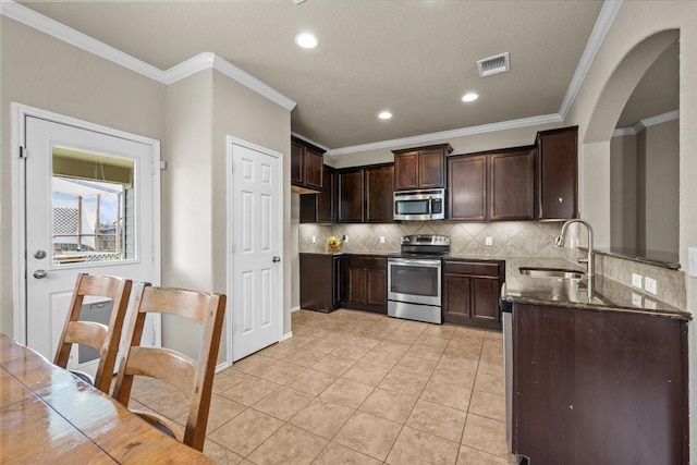 9444 Centennial Dr, Waco, TX 76708 - kitchen with stainless steel appliances, dark stone counters, tasteful backsplash, dark brown cabinetry, and ornamental molding