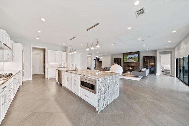 4441 Amherst Ave, University Park, TX 75225 - kitchen featuring appliances with stainless steel finishes, a lit fireplace, a large island, white cabinets, and light stone countertops