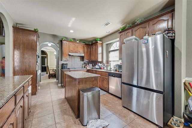 461 Running Water Trl, Fort Worth, TX 76131 - kitchen with appliances with stainless steel finishes, decorative backsplash, arched walkways, a kitchen island, and light stone counters