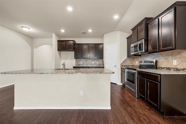 3217 Beutel Rd, Lorena, TX 76655 - kitchen featuring appliances with stainless steel finishes, light stone counters, dark brown cabinetry, a kitchen island with sink, and decorative backsplash