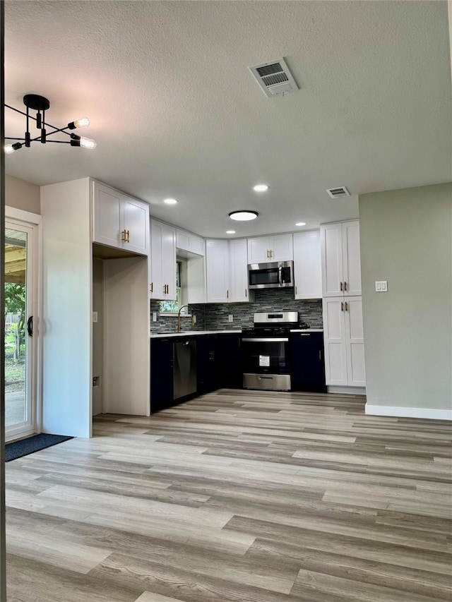 3633 Flamingo Way, Mesquite, TX 75150 - kitchen with appliances with stainless steel finishes, white cabinets, decorative backsplash, light wood-style floors, and a textured ceiling