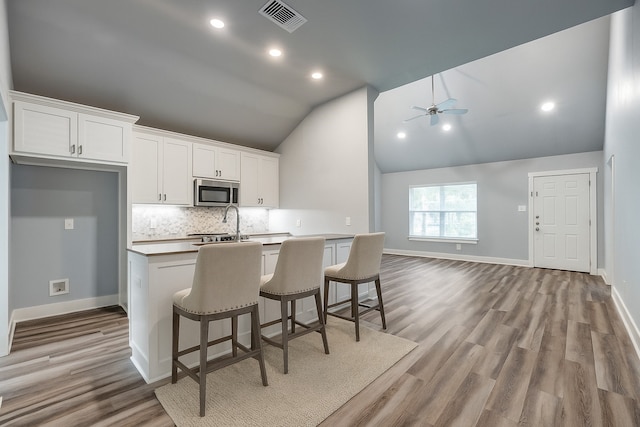 606 E 12th St, Bonham, TX 75418 - kitchen featuring stainless steel microwave, an island with sink, ceiling fan, white cabinetry, and tasteful backsplash