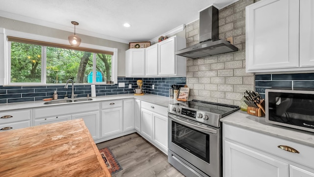 307 Bryan St, Weatherford, TX 76086 - kitchen featuring wall chimney range hood, appliances with stainless steel finishes, decorative backsplash, white cabinetry, and ornamental molding