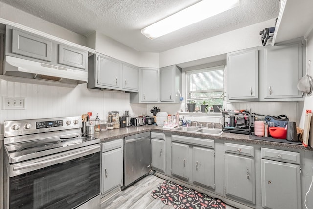 1106 Sunnyvale Dr, Arlington, TX 76010 - kitchen with stainless steel appliances, under cabinet range hood, a textured ceiling, light wood-style floors, and gray cabinetry