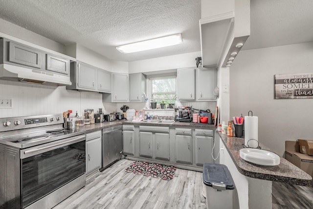 1106 Sunnyvale Dr, Arlington, TX 76010 - kitchen with appliances with stainless steel finishes, under cabinet range hood, dark countertops, a textured ceiling, and light wood-style flooring