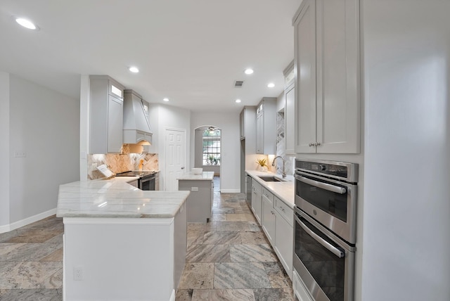 4418 Spring Garden Dr, Arlington, TX 76016 - kitchen featuring stainless steel appliances, custom range hood, stone tile floors, a peninsula, and decorative backsplash