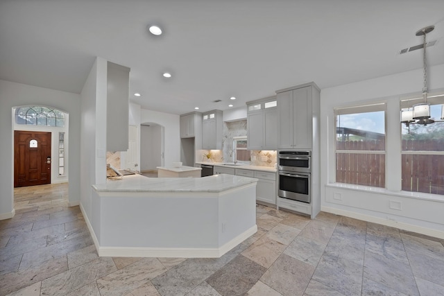 4418 Spring Garden Dr, Arlington, TX 76016 - kitchen featuring stone tile flooring, appliances with stainless steel finishes, decorative backsplash, a peninsula, and glass insert cabinets