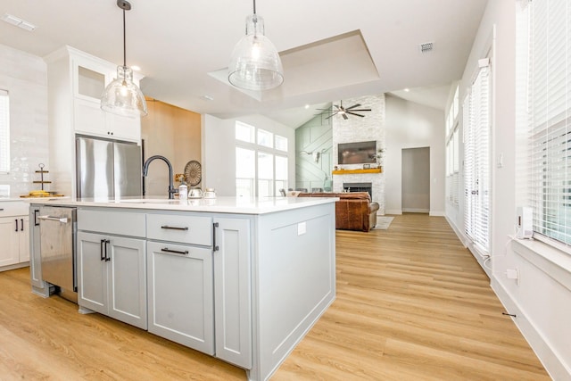 9209 Old Stoney Rd, Ponder, TX 76259 - kitchen with appliances with stainless steel finishes, a ceiling fan, a kitchen island with sink, a fireplace, and light wood-type flooring