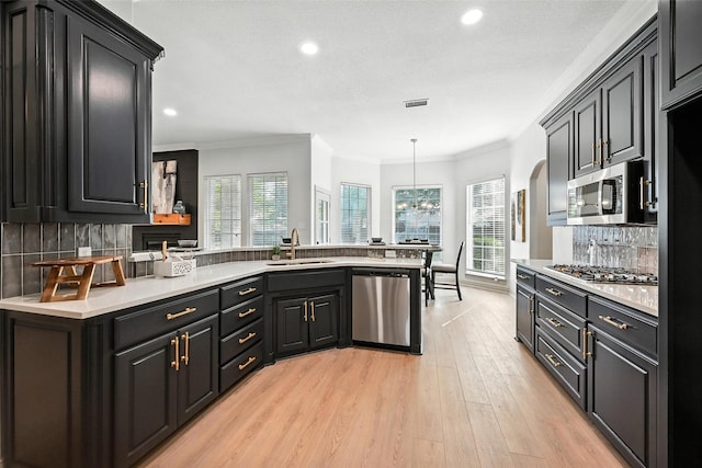 901 Bluebird Ct, Burleson, TX 76028 - kitchen featuring appliances with stainless steel finishes, a peninsula, plenty of natural light, light wood-style flooring, and ornamental molding
