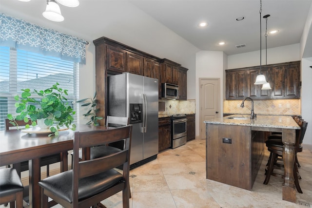 306 Spruce Trl, Forney, TX 75126 - kitchen featuring stainless steel appliances, backsplash, light stone counters, dark brown cabinets, and an island with sink