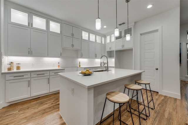 1403 Pueblo St, Dallas, TX 75212 - kitchen with light wood finished floors, a center island with sink, glass insert cabinets, decorative backsplash, and recessed lighting