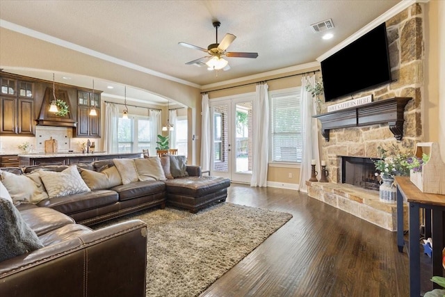 2213 Therese Dr, Waco, TX 76712 - living room featuring a ceiling fan, crown molding, dark wood-style flooring, a stone fireplace, and arched walkways