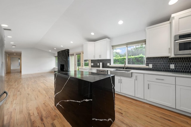 5710 Forest Ln, Dallas, TX 75230 - kitchen with lofted ceiling, light wood finished floors, tasteful backsplash, a kitchen island, and white cabinets