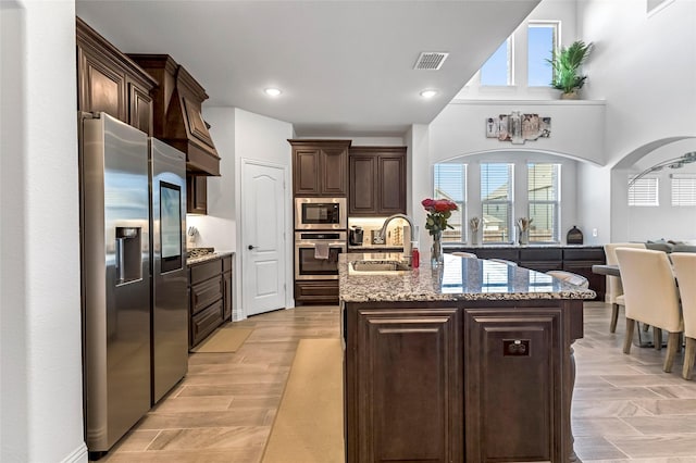 303 Hidden Cove Dr, Ponder, TX 76259 - kitchen with stainless steel appliances, dark brown cabinets, light stone counters, a center island with sink, and recessed lighting
