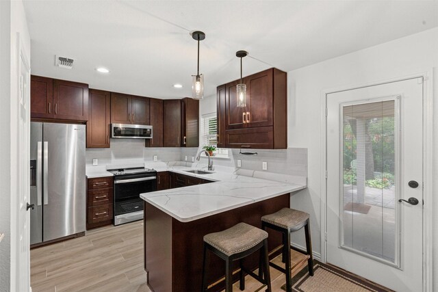 9013 Topperwind Ct, Fort Worth, TX 76134 - kitchen featuring appliances with stainless steel finishes, a peninsula, backsplash, dark brown cabinets, and pendant lighting